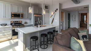 Una cocina moderna con una isla central, taburetes de bar y una zona de comedor con un sofá y cojines marrones.