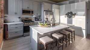 A modern kitchen with white cabinets, a central island with stools, a brick wall, and a ceiling with a decorative design.