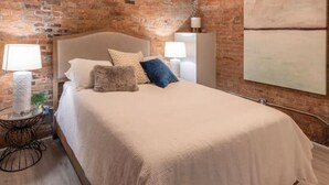 A bedroom with a brick wall, a bed with white bedding, two bedside lamps, and a modern ceiling light.