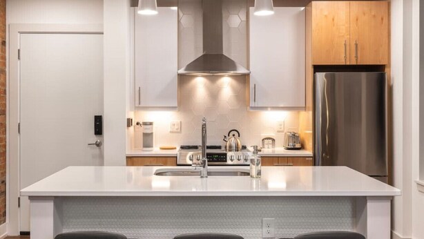 Une cuisine moderne dotée d’un îlot central, d’appareils électroménagers en acier inoxydable et de luminaires suspendus.