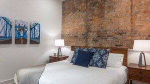 Une chambre avec un lit en bois, deux tables de chevet, un ventilateur de plafond et un mur en briques.