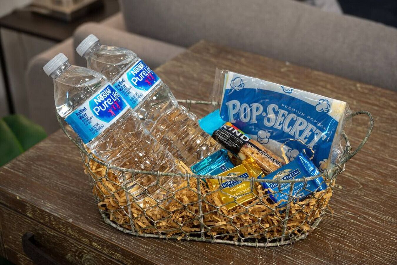 A wire basket containing two bottles of Nestlé Pure Life water, a pack of Pop Secret Popcorn, and some chocolate bars.