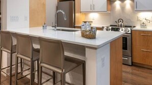 Une cuisine moderne dotée d’un îlot central, de tabourets de bar, d’appareils électroménagers en acier inoxydable et de meubles de rangement en bois.