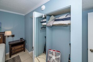 Ein Schlafzimmer mit Bett, Nachttisch, Lampe und begehbarem Kleiderschrank inklusive Ventilator und Kleiderstange.