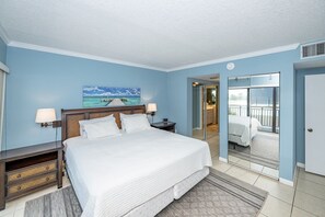 Quarto de hotel com uma cama grande, uma mesa de cabeceira, um abajur, um quadro de um cais e vista para uma varanda.