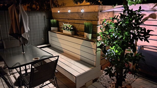 Un patio con una mesa y sillas de vidrio, un banco de madera y una planta en maceta.