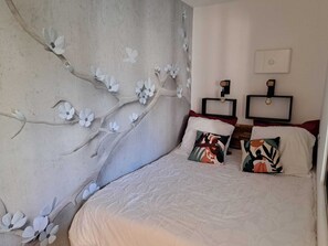 Een slaapkamer met een groot bed, twee nachtkastjes, een wandtelevisie en een decoratieve muur met witte bloemen.