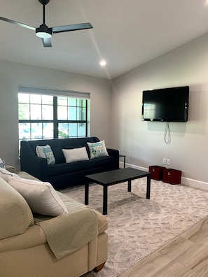 A living room with a dark blue sofa, beige couch, and a flat-screen TV mounted on the wall.