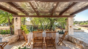 An outdoor patio with stone flooring, wooden chairs, a table, and a pergola. - Trullo La Succulenta - Le Case di Valentina (Ceglie Messapica)