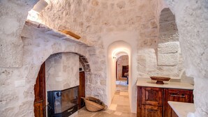 A stone-walled kitchen with a fireplace, wooden cabinets, and a stone floor. - Trullo La Succulenta - Le Case di Valentina (Ceglie Messapica)