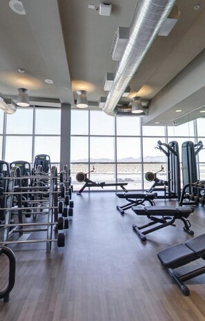 Een sportschool met diverse trainingsapparaten, grote ramen en uitzicht op een woestijnlandschap.