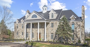 A large stone house with a central entrance, multiple chimneys, and a large window with a fan design. - Beautiful Bluemont Estate (Bluemont)