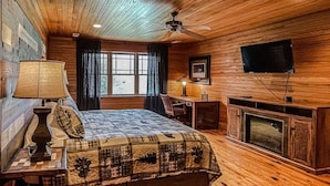 A wooden-paneled bedroom with a bed, a desk, a television, and a fireplace.