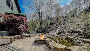 A patio area with a fire pit, wooden benches, and a small pond.