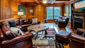 A cozy log cabin interior with leather furniture, a fireplace, and large windows.