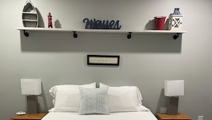 A bedroom with a bed, two bedside tables, a shelf with decorative items, and a framed quote on the wall. - Getaway St Andrews - Bright Spacious Vacation Home (St. Andrews)