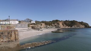Eine Küstenlandschaft mit einer Steinmauer, einem Sandstrand und einer Felsküste.