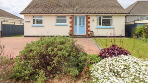 Ein eingeschossiges Haus mit Ziegeldach, einer blauen Haustür und einem kleinen Garten mit verschiedenen Pflanzen und Blumen.