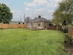 A stone house with a fenced backyard, a picnic table, and a small deck.