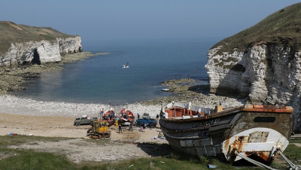 A coastal scene with a boat named 'SPRING FLOWER' docked on a sandy beach, cliffs in the background, and a clear blue sky. - Westfield (Bridlington)