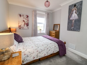 A bedroom with a bed, a dresser, a lamp, a window with curtains, and a painting on the wall.