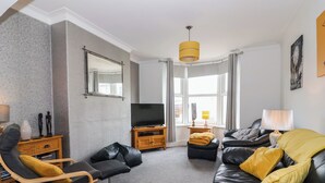 A modern living room with a leather sofa, a wooden chair, a TV, and a large window. - Westfield (Bridlington)