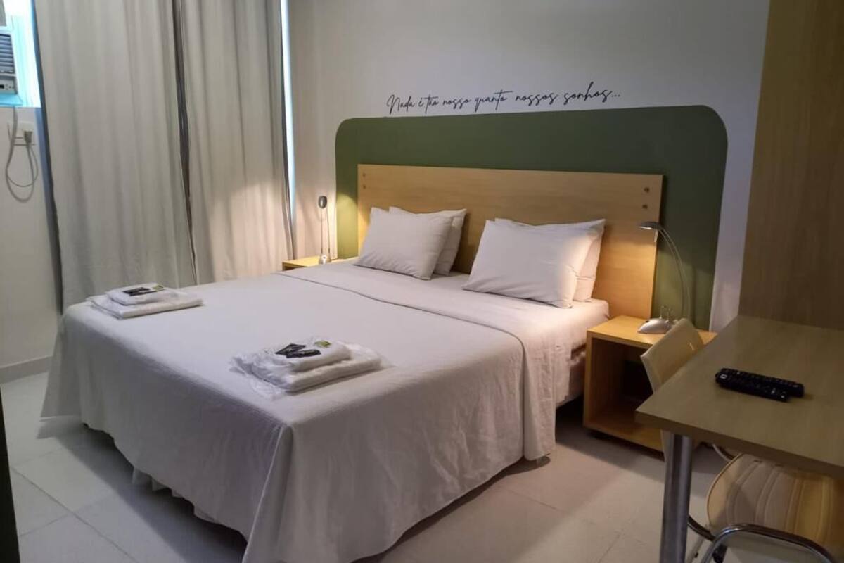 A hotel room with a bed, a bedside table, a chair, and a desk with a keyboard.