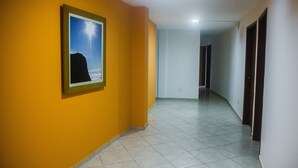 Un pasillo con un cuadro enmarcado en la pared, suelo de baldosas y puertas a la derecha.