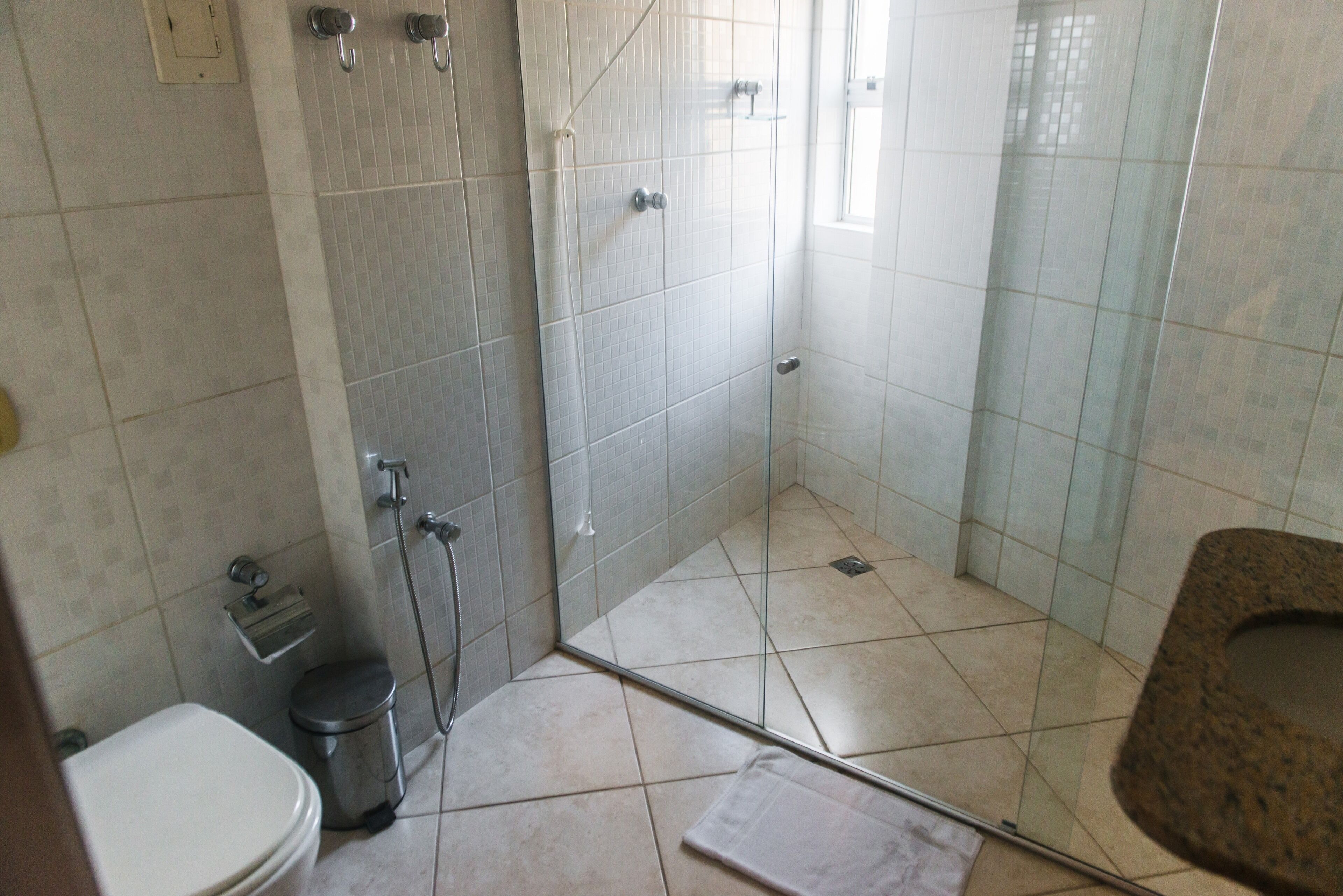 A bathroom with a toilet, a trash bin, a shower with glass doors, and a sink.