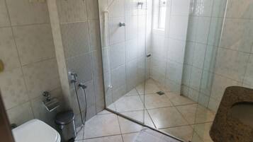 A bathroom with a toilet, a trash bin, a shower with glass doors, and a sink.
