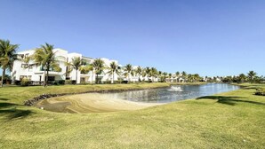 Un parcours de golf avec un obstacle d’eau, des palmiers et un bâtiment à la façade blanche.