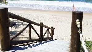 Une promenade en bois mène à une plage de sable, avec l’océan et ses vagues en arrière-plan.
