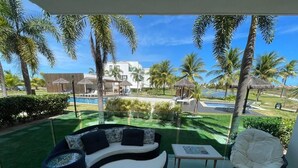 Un balcon avec un canapé, une chaise et une petite table, donnant sur une piscine et des palmiers.