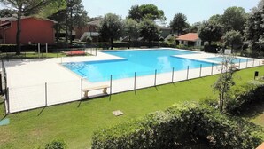 Ein rechteckiger Pool mit weißem Sonnendeck und Umzäunung, umgeben von gepflegtem Rasen und Bäumen.