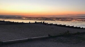 Een strand met een houten looppad dat naar het water leidt, een lage muur en een heldere lucht.