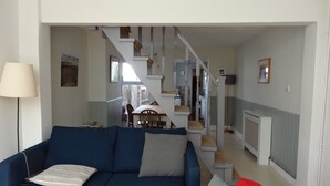 Een woonkamer met een blauwe bank, een rode bank, een lamp en een trap naar een eetgedeelte.