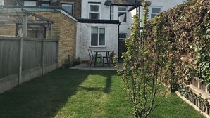 Een woonhuis met een verzorgd gazon, een kleine tuin en een patio met buitenmeubilair.