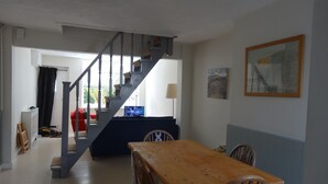 Een eetgedeelte met een houten tafel en stoelen, een trap en een bank op de achtergrond.