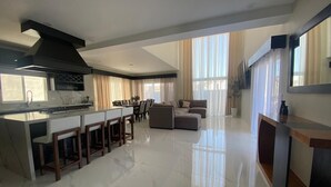 Cocina moderna con una isla central, zona de comedor con mesa y sillas, y sala de estar con sofá.