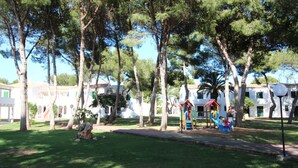 A park with playground equipment, trees, and white buildings in the background.