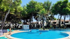 A swimming pool surrounded by lounge chairs and palm trees, with a building in the background.