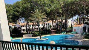 A balcony with a view of a swimming pool, surrounded by trees and buildings.