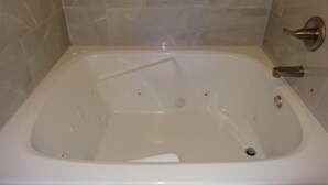 A white bathtub with a built-in seat, a handheld showerhead, and a wall-mounted faucet.