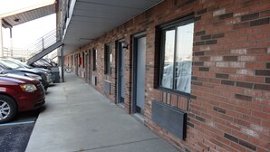 A row of parked cars along a brick building with large windows and a covered walkway.