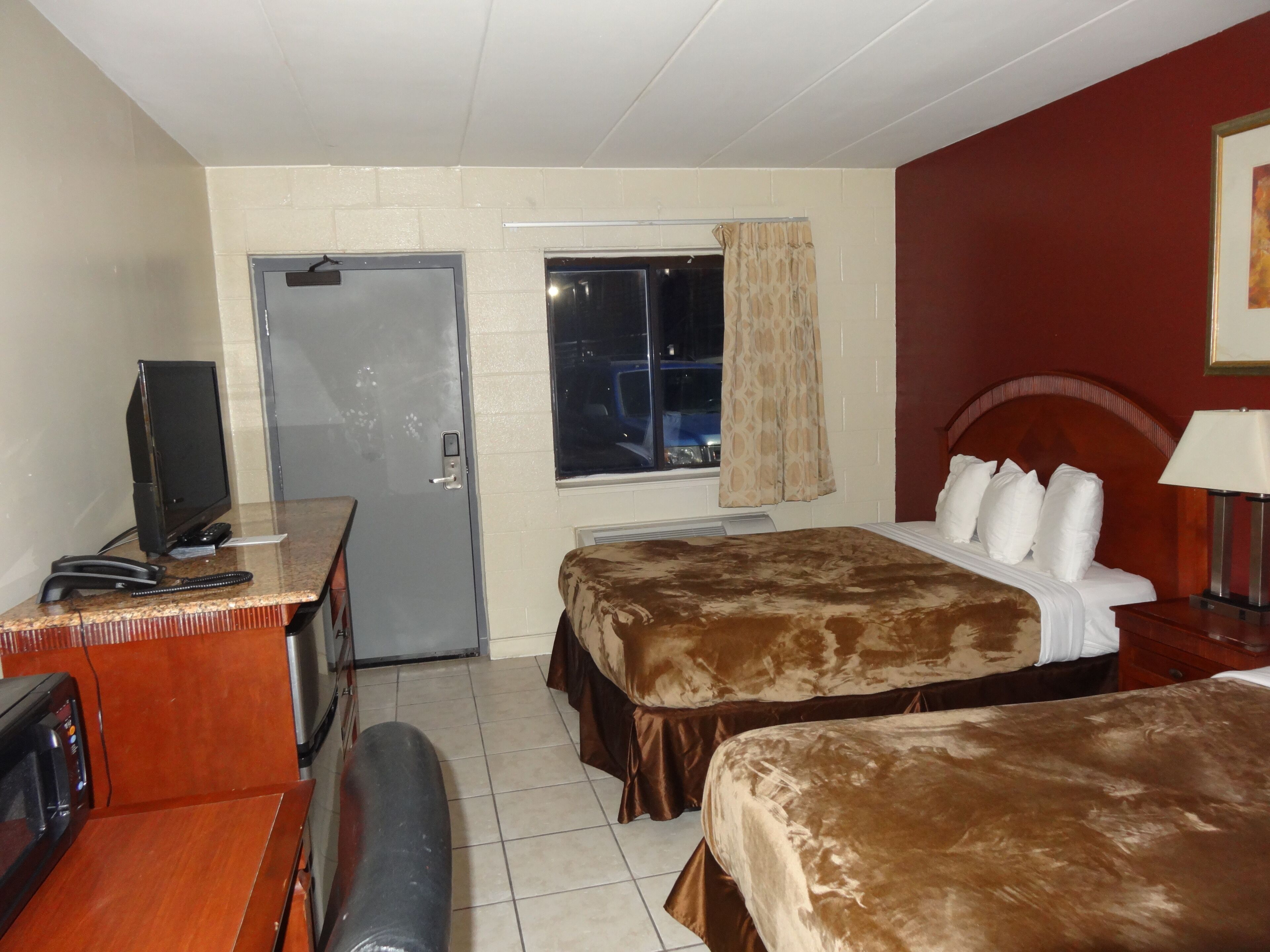 A hotel room with two beds, a desk with a television, a microwave, and a door with a window.