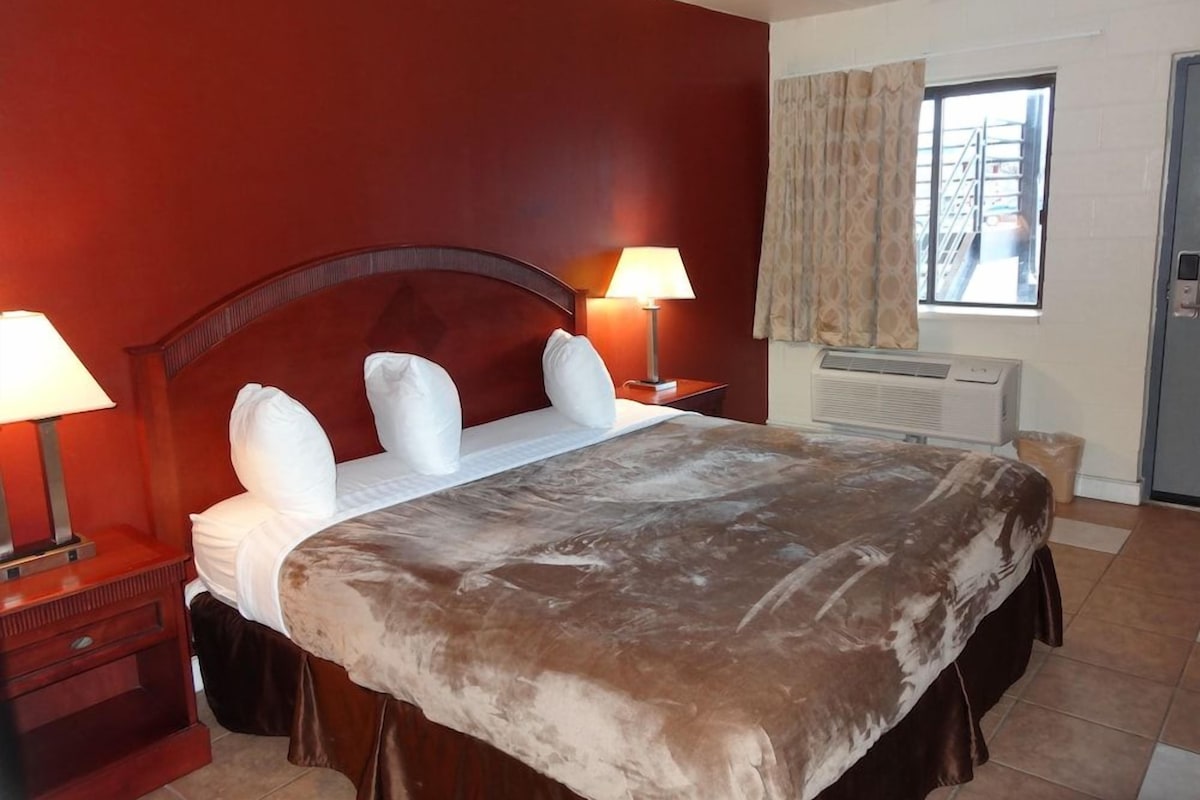 A hotel room with a large bed, two bedside tables with lamps, a window with curtains, and a radiator.