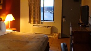 A hotel room with a bed, two bedside lamps, a window with curtains, a radiator, and a TV on a stand.