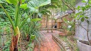 Un sendero de ladrillos que atraviesa un jardín exuberante con diversas plantas y una valla de madera al fondo.