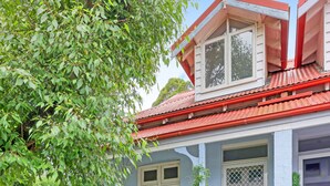 Una casa con techo rojo, paredes blancas y un porche delantero.