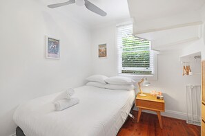 A bedroom with a bed, a desk, a lamp, and a window with blinds.